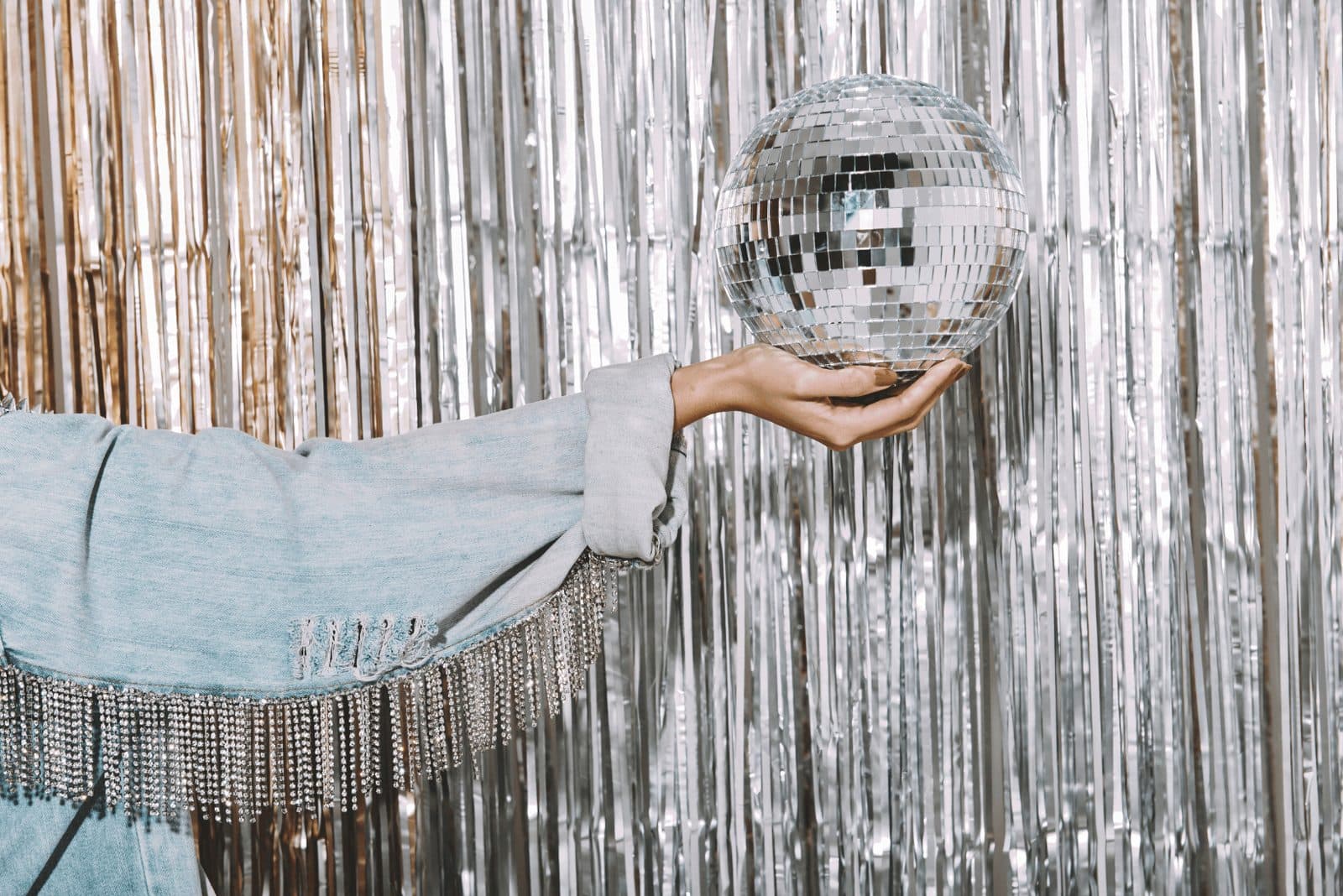 A hand holding a disco ball against a silver tinsel backdrop in a styled photo shoot
