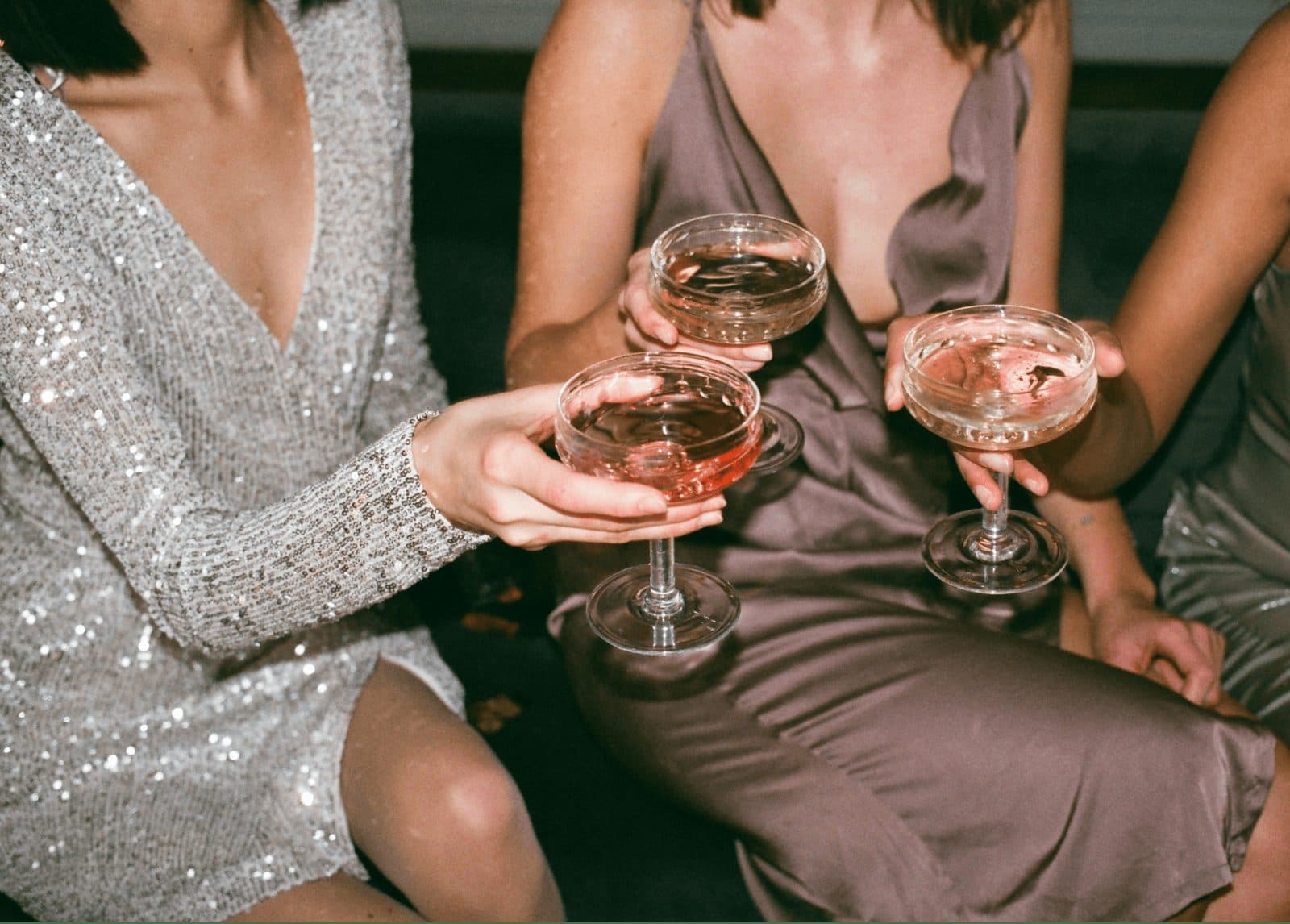 Friends in sequins and satin toasting with coupe glasses