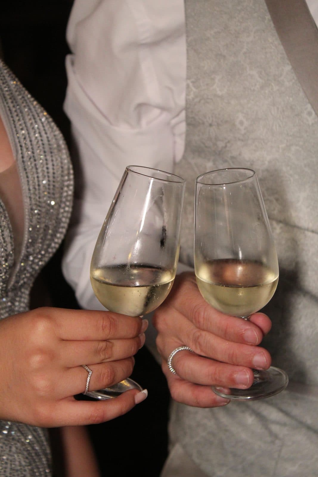 A couple toasting with white wine, an engagement ring on her hand