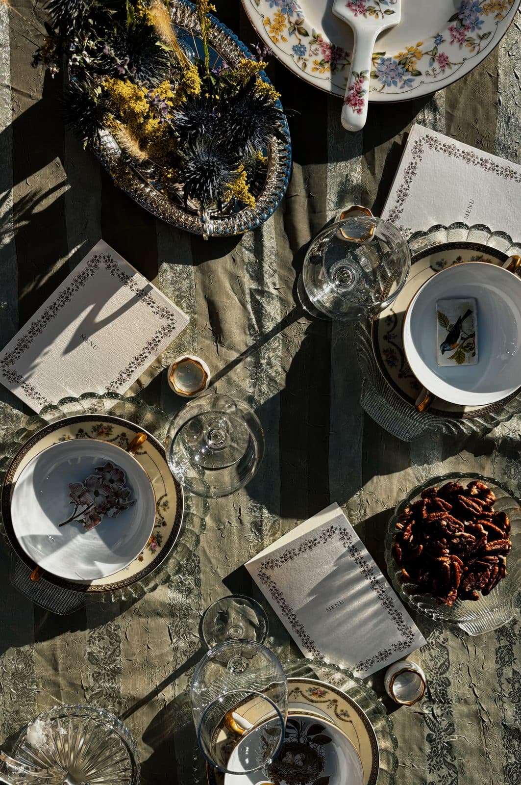 A table set with printed menu cards, patterned china and glassware seen from above