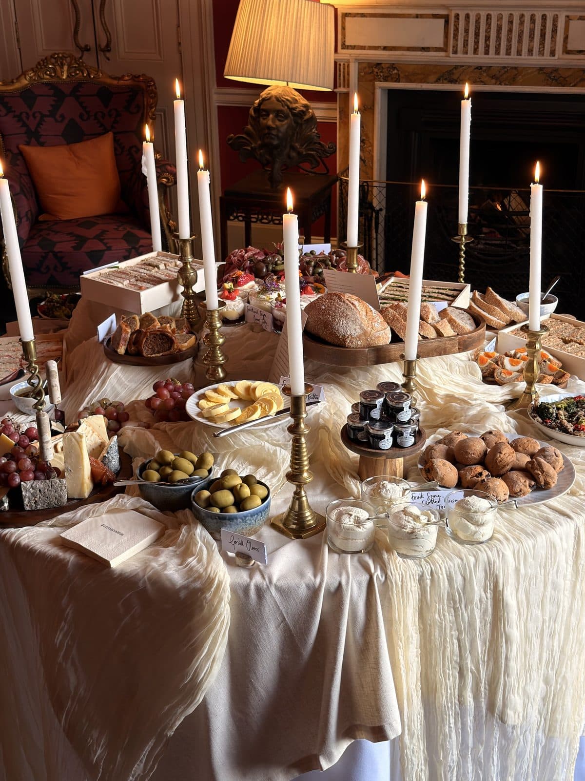 A candlelit grazing table with breads, cheeses and desserts on draped linen