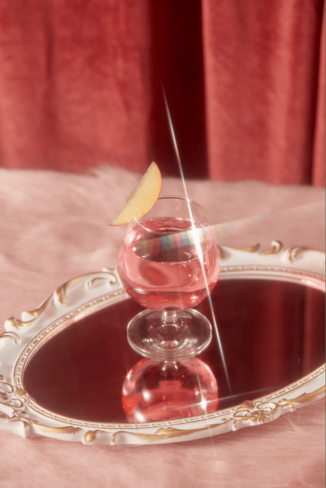A pink signature cocktail with a citrus twist on a mirrored vintage tray