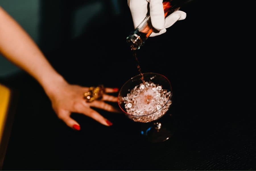 A cocktail being poured into a coupe glass at a wedding bar