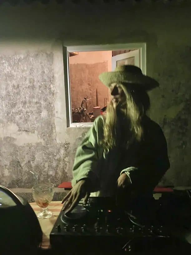 A DJ in a straw hat mixing at the decks beside a cocktail glass at an evening party