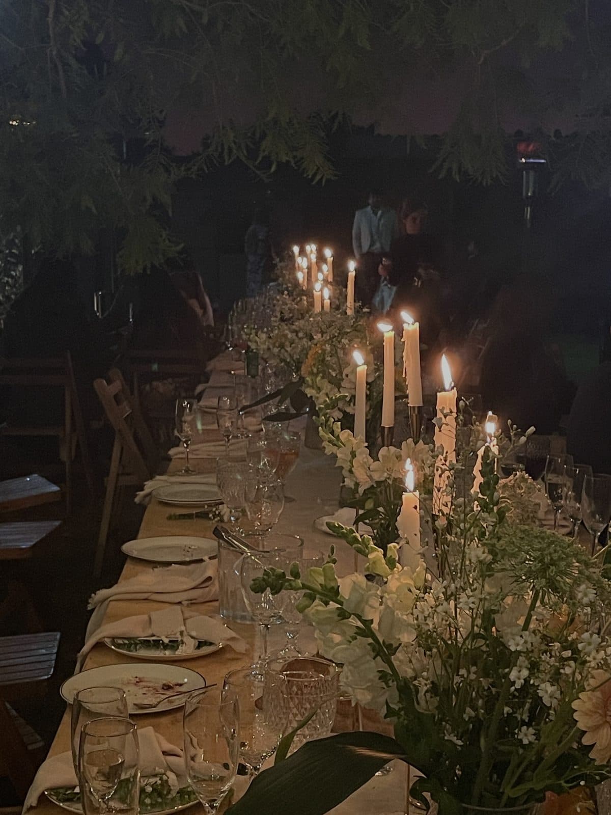 A long reception table lined with lit taper candles and white flowers at night