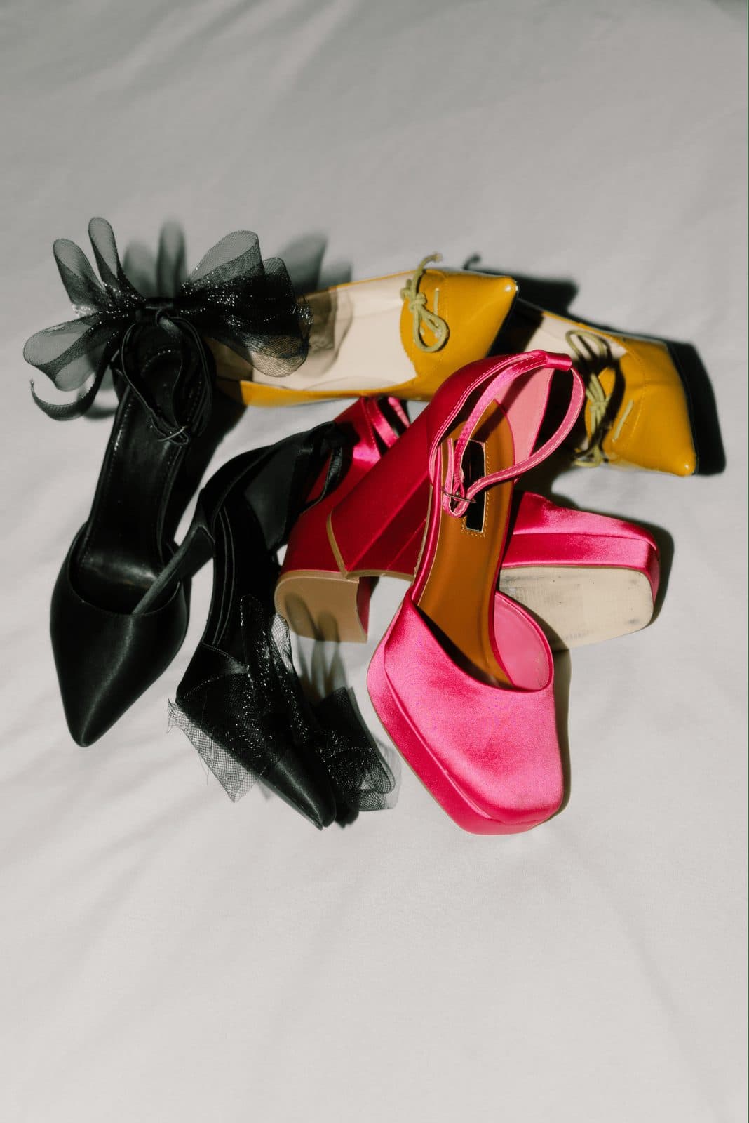 Black, pink and mustard wedding heels piled together on white linen