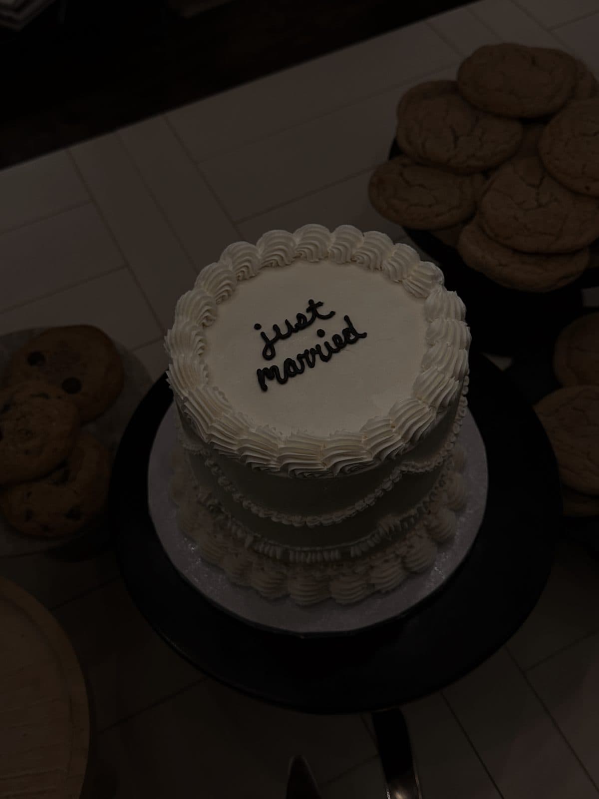 A small white wedding cake piped with the words just married, on a dessert table with cookies